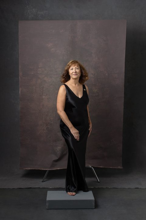 Studio portrait of Karen wearing a long black dress, in front of two backdrops