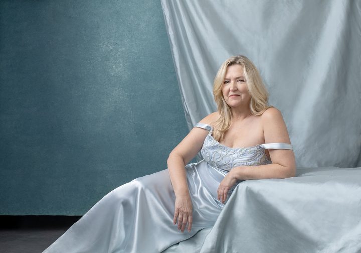 Portrait of MaryEllen, reclining, wearing a light blue gown in front of a layered light blue background