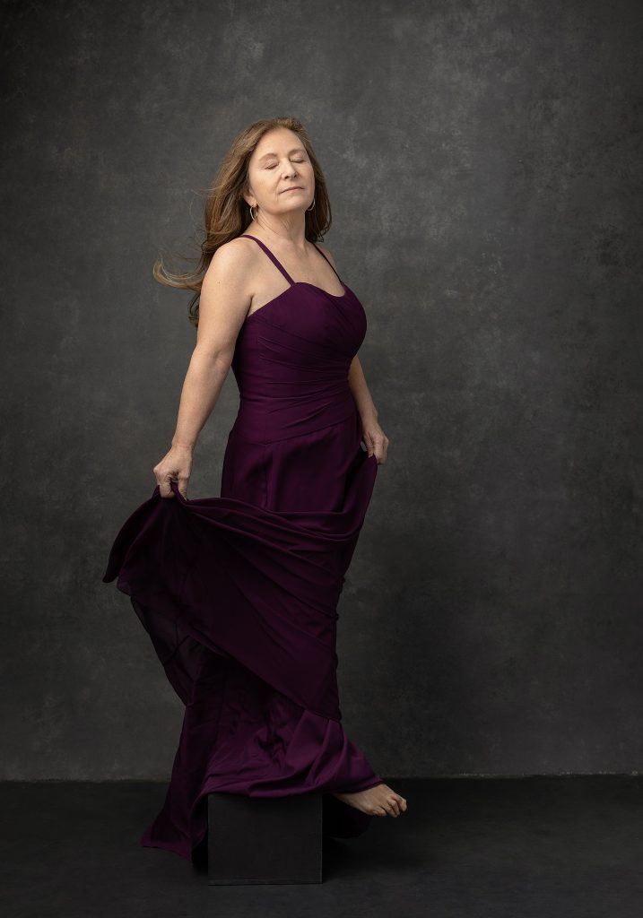 Portrait of Kathy wearing a purple gown with her eyes closed, as part of her portrait session for Extraordinary: the Over 50 Revolution