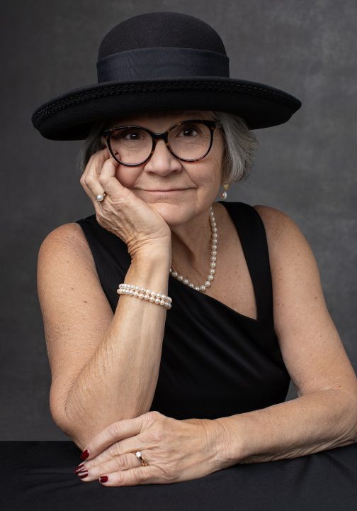 Portrait from Extraordinary: the Over 50 Revolution - Rebecca wearing a black hat, leaning on a table