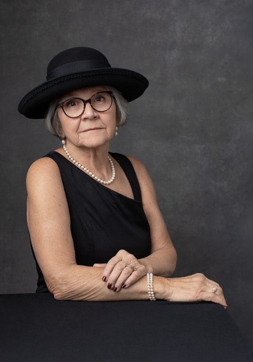 Portrait from Extraordinary: the Over 50 Revolution - Rebecca wearing a black hat, leaning on a table