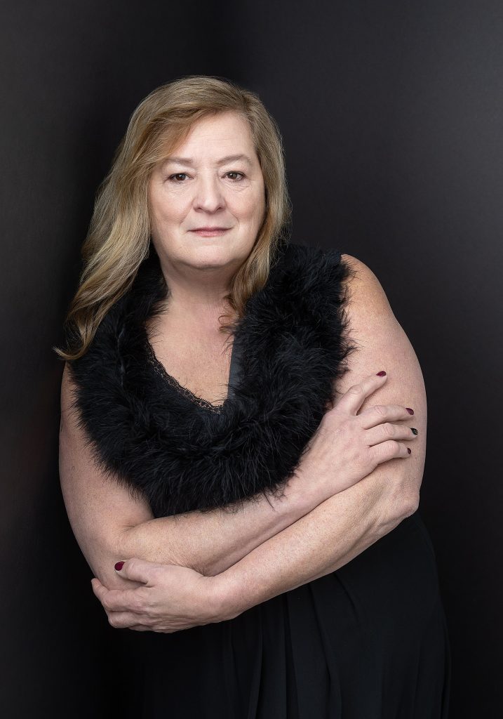 Portrait of Robin wearing a black dress in front of a black background as part of her photo session for the Over 50 Revolution 2023