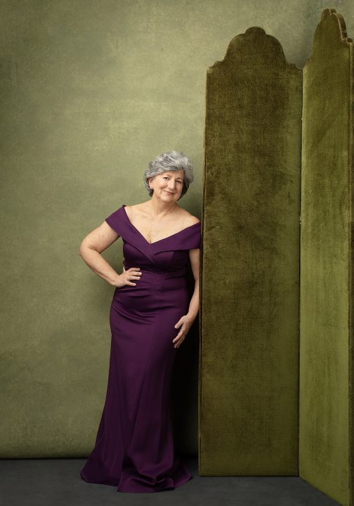 Portrait of Susan C. wearing a purple gown in front of green set for her Over 50 Revolution photo session