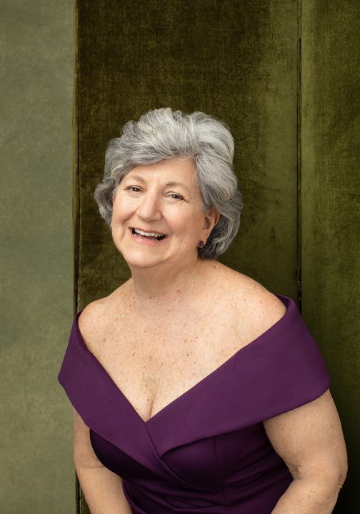 Portrait of Susan C. wearing a purple gown in front of green background