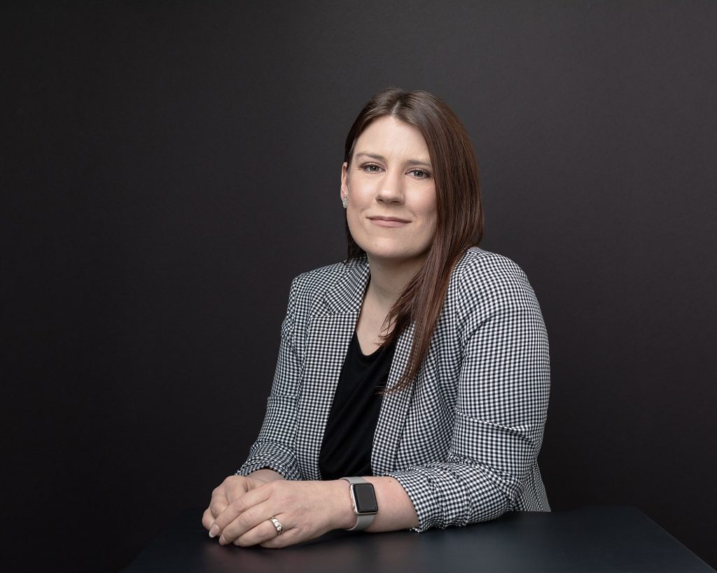 Business portrait of Ashley, seated with black background