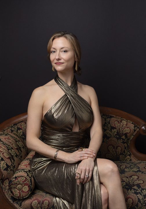 Portrait of Claire, wearing a gold gown, sitting on an antique sofa