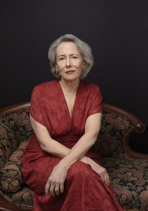 Portrait of Jean, wearing a rust-colored gown, sitting on an antique sofa