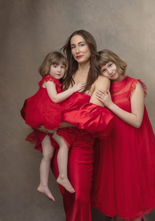 Portrait of mother and two young daughters wearing red dresses