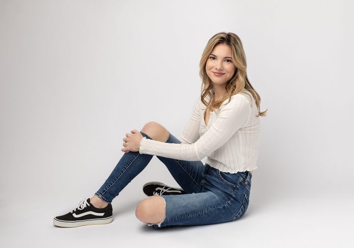 Casual senior photo of Brianna, sitting on floor, wearing jeans and sneakers