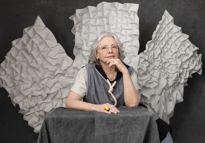 Portrait of Kathy, seated, with her artwork hanging behind her.