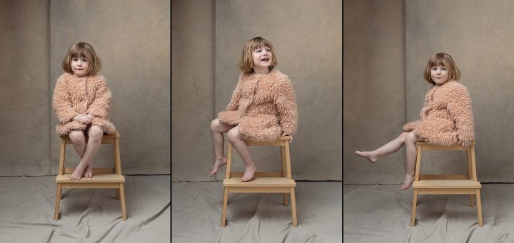 Portraits of a young child sitting on a stool, wearing a fluffy pink coat