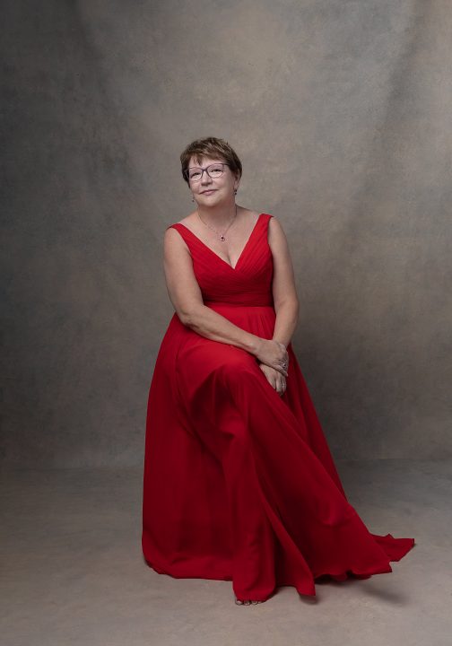 Portrait of Karen seated, wearing a red dress for her photo session for Extraordinary: the Over 50 Revolution