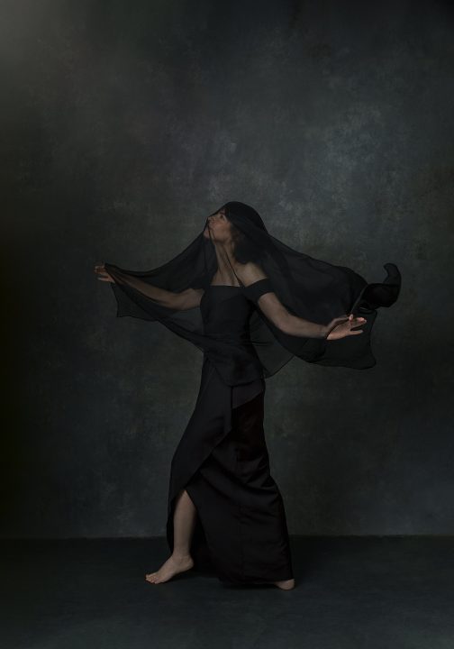 A portrait of Karen, wearing a black gown with flying fabric