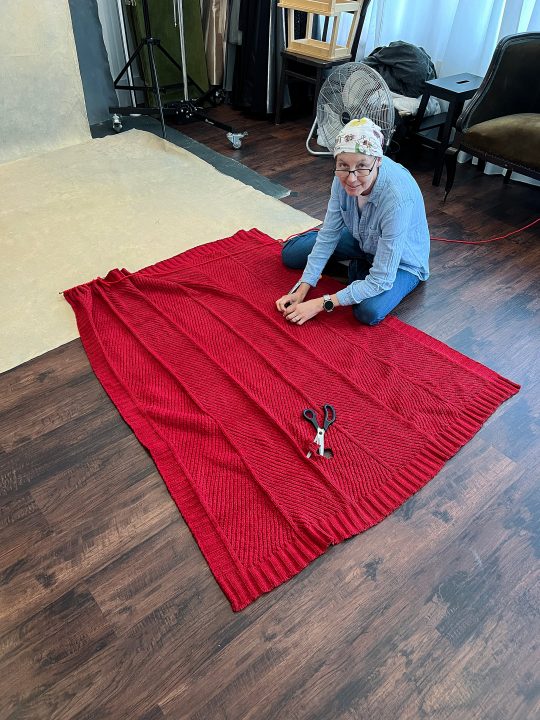 Behind the scenes cell photo of Jody helping to prepare her knitted garment for her portrait for Knitted Together, Part V