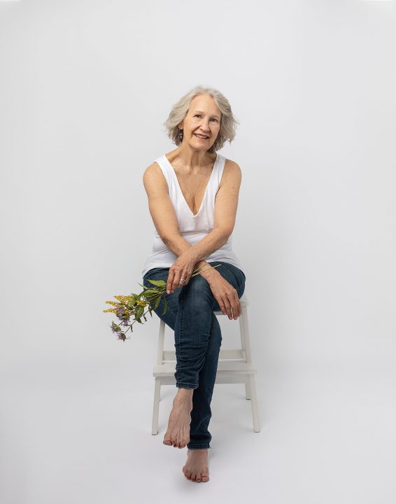 Judith, seated in front of a white backdrop, holding wildflowers