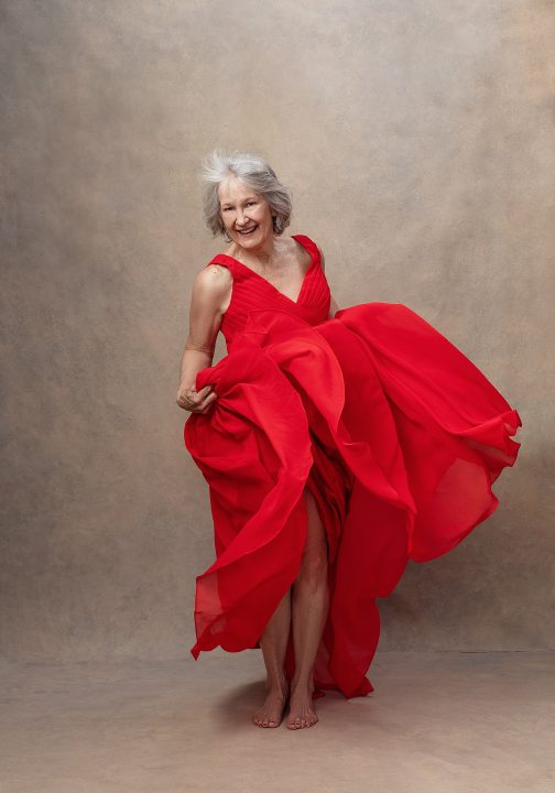 Portrait of Judith, dancing joyfully, wearing a red dress during her session for Extraordinary: the Over 50 Revolution