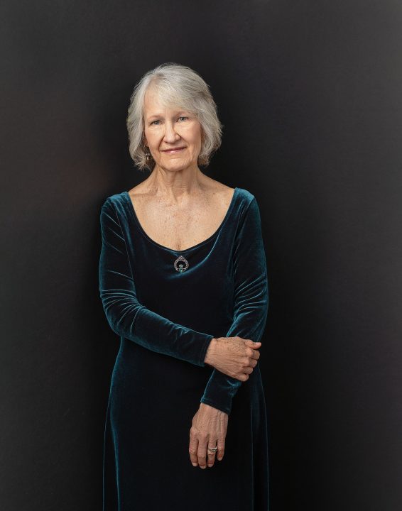 Portrait of Judith for Extraordinary: the Over 50 Revolution. She is wearing a velvet dress, in front of a black backdrop.