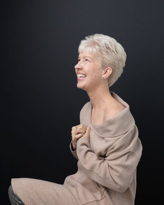 Portrait of Debbie, laughing, with a black background, for Extraordinary: the Over 50 Revolution