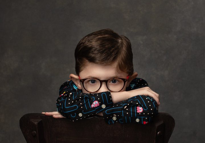 A portrait of a young boy wearing glasses and a Pac Man shirt