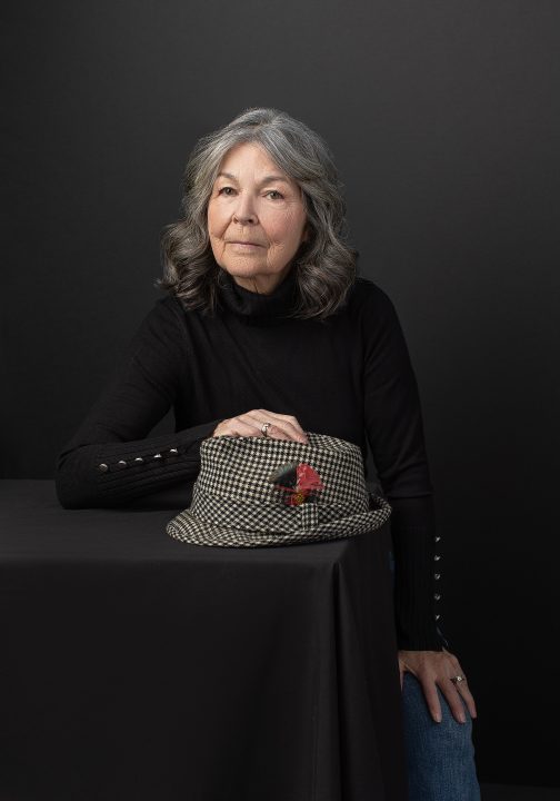 Portrait of Deb, seated with a hat, wearing a black turtleneck