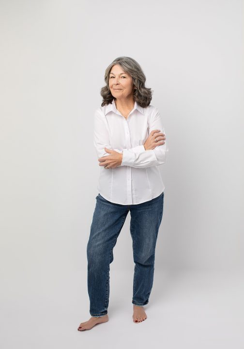 Portrait of Deb, barefoot, wearing white shirt and jeans for The Over 50 Revolution