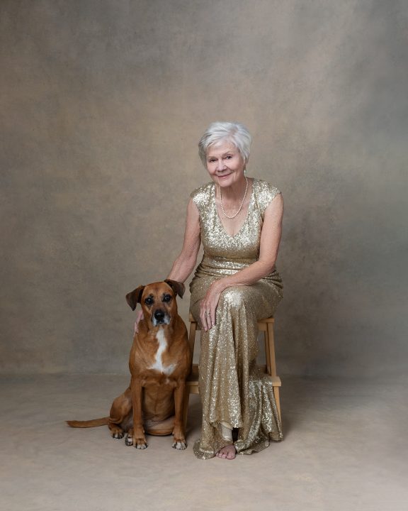 Portrait of Sharon wearing a gold gown, sitting with her dog for the Over 50 Revolution