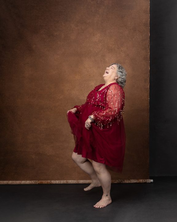 Maria, dancing and laughing, wearing a red dress during her portrait session for The Over 50 Revolution