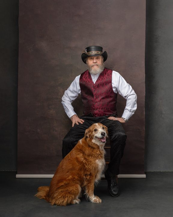 Photo of Mark wearing steampunk hat and vest, with dog Marley