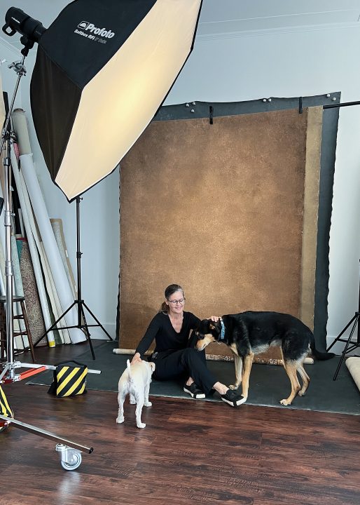 Behind the scenes photo of Maundy, sitting on the floor with Patty & Dan's two dogs