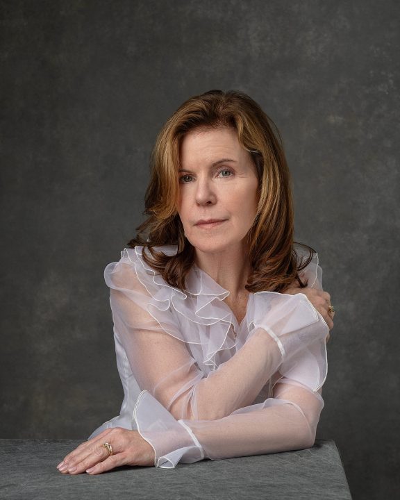 A portrait of Debra, seated at a table, wearing a sheer tulle blouse