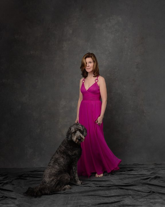 A portrait of Debra, wearing a long pink dress with her dog sitting beside her, during her photo session for The Over 50 Revolution