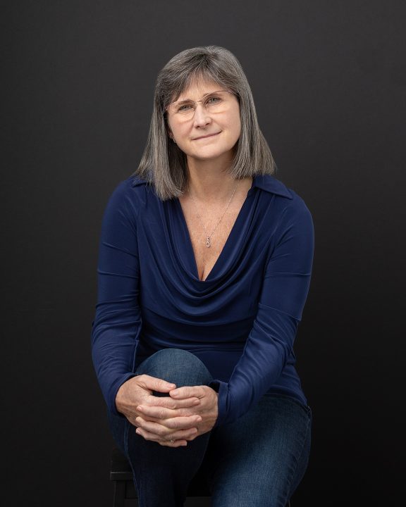 A branding portrait for Physical Therapist Melinda Johnston. She is seated against a black background
