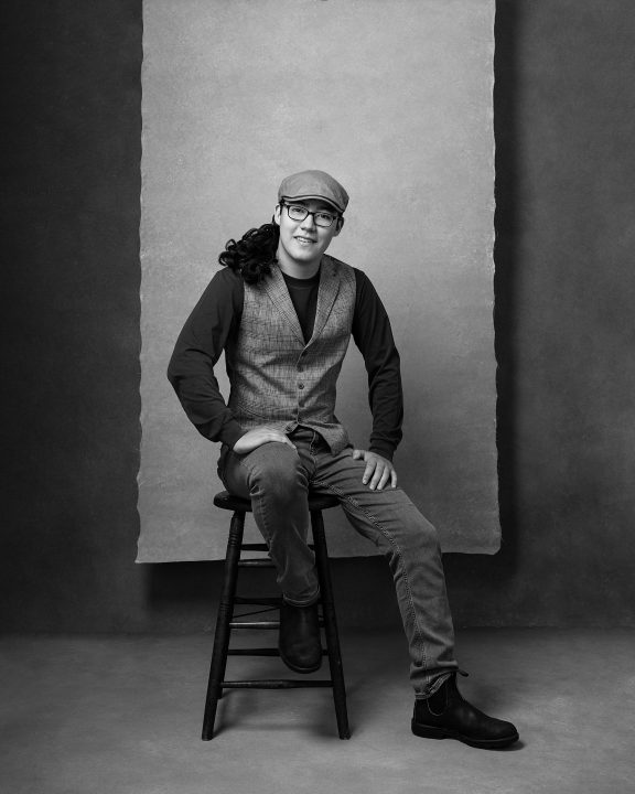 Black and white portrait of David, seated, wearing a cap