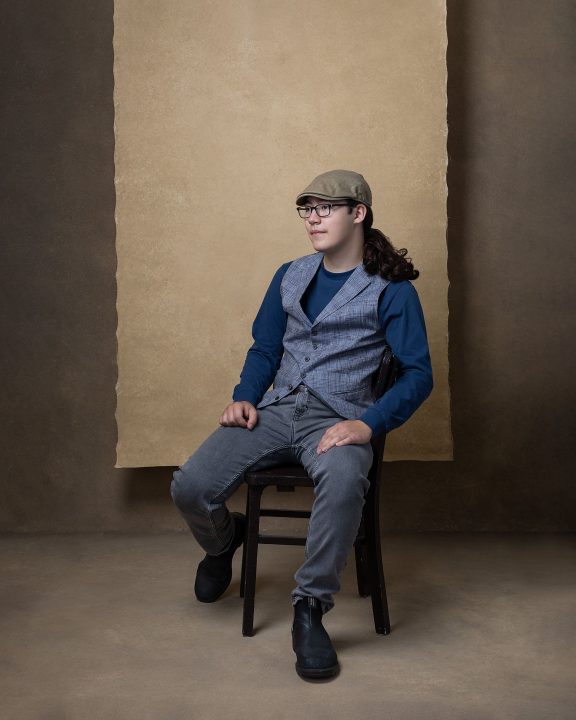 Portrait of David at 18, seated, wearing a cap, looking away from the camera