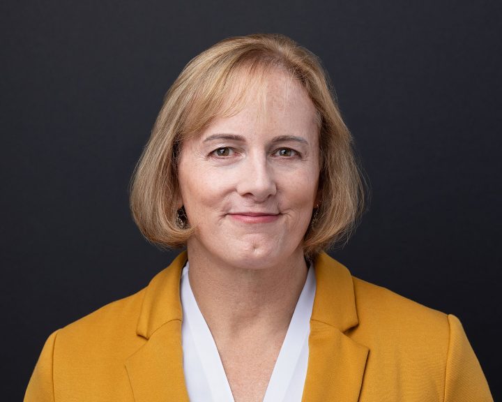 A headshot for entrepreneur Jess, who is wearing a gold blazer, in front of a black backdrop