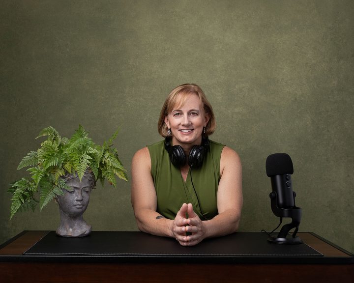 Jess, a diversity-focused entrepreneur with a punk spirit, seated at a desk ready for her podcast, in front of a green background