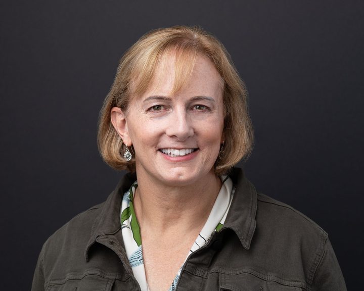 A headshot for entrepreneur Jess, who is smiling in front of a black backdrop