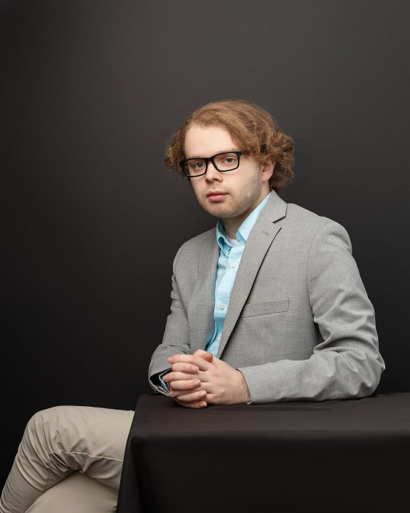 Professional headshot for new graduate from PSU, Michael. He is seated in front of a black background