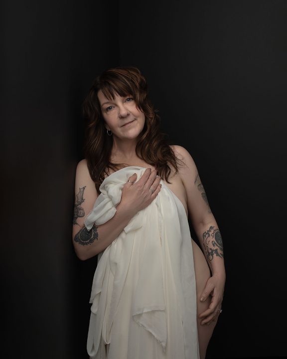 Portrait of a woman holding cream colored fabric in front of a black background