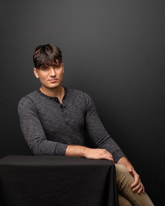 A portrait of Maxwell sitting in front of a black backdrop for his first modeling portfolio