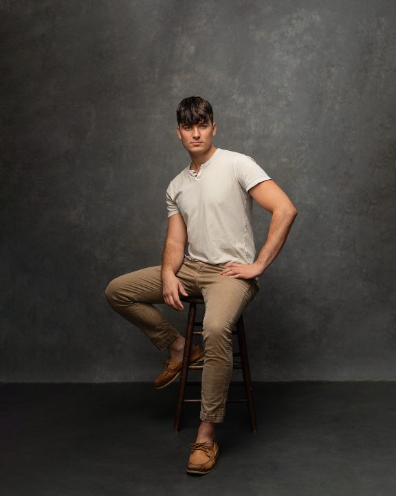 A full-body portrait of Maxwell, seated in front of a gray backdrop for his first modeling portfolio
