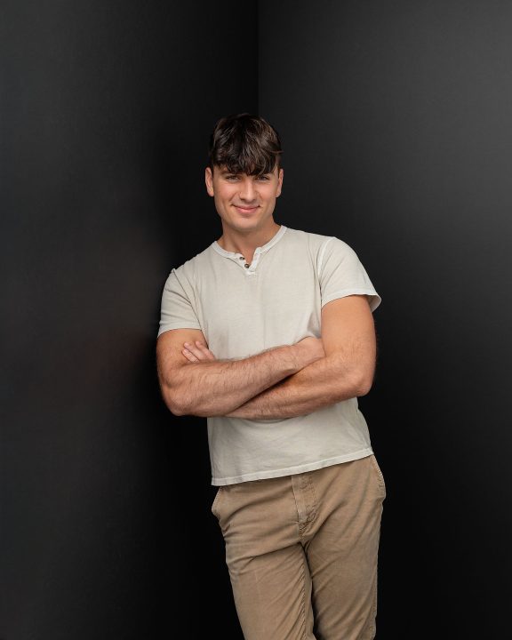 A three-quarter-body photo of Maxwell, leaning against a black background for his first modeling portfolio