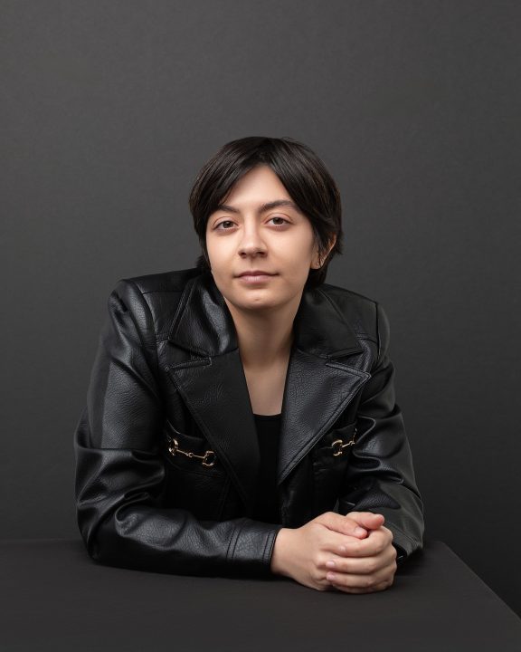 An acting headshot / portrait for Tori. She is seated at a table in front of a black background