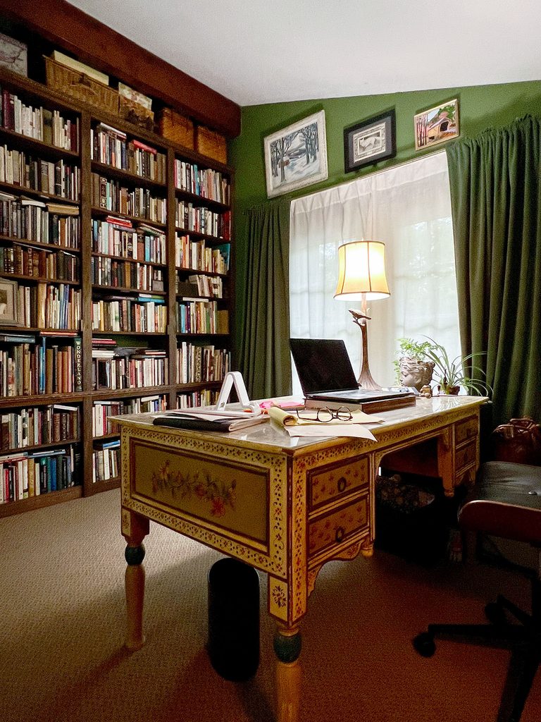 Photo of Maundy Mitchell's writing space, with tall bookshelves and a painted desk